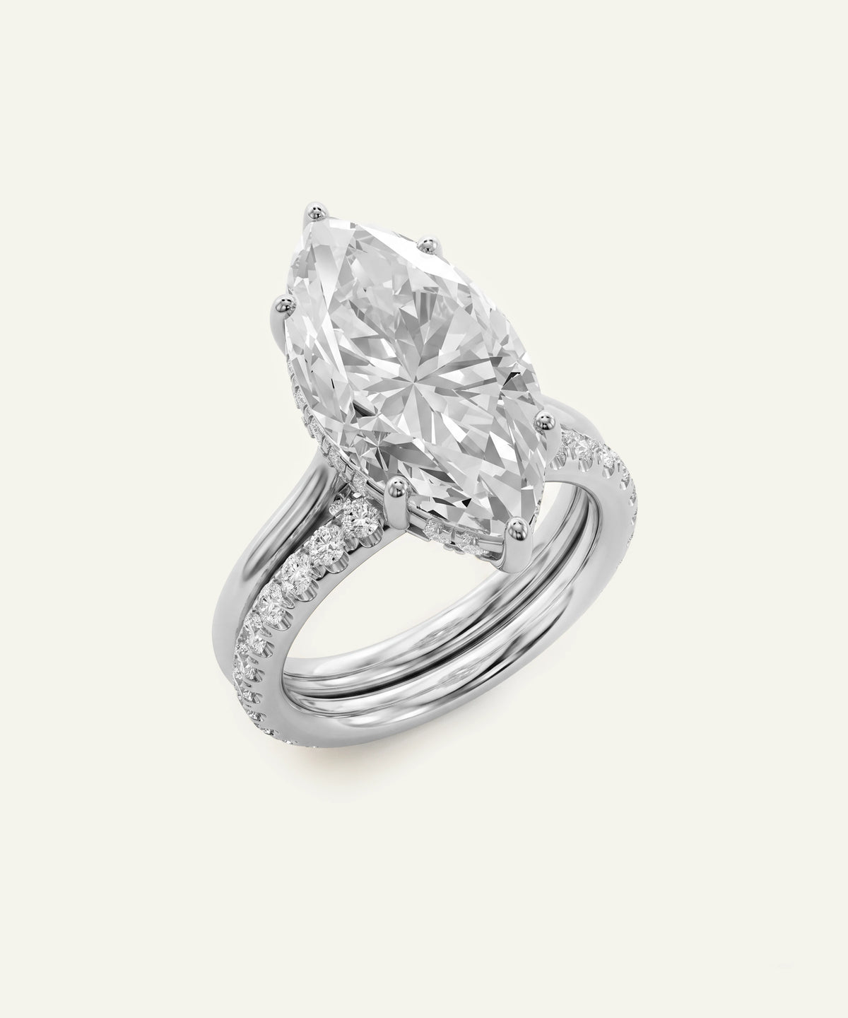 A silver-tone ring featuring a large marquise-cut clear gemstone in a prong setting, with a split shank accented by small pavé stones, shown on a light cream background.