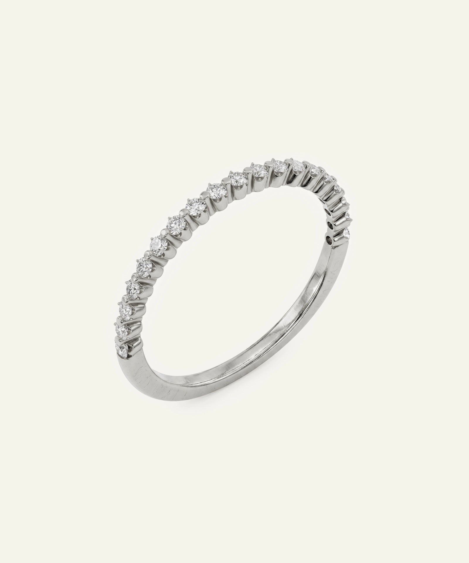 A silver-toned eternity ring featuring a row of small clear round-cut stones set along the band, photographed on a solid off-white background.
