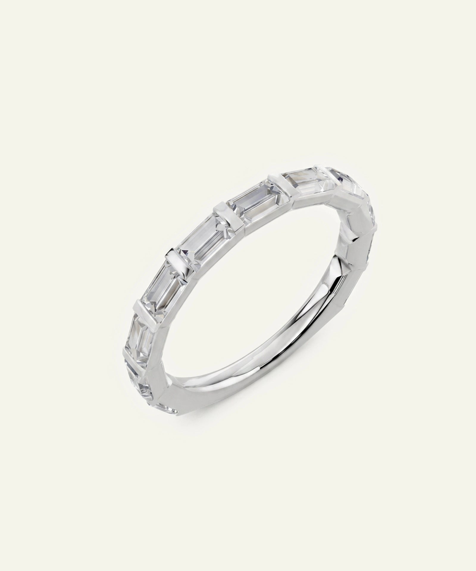 A silver band ring featuring a row of baguette-cut clear gemstones, photographed on a light cream background.