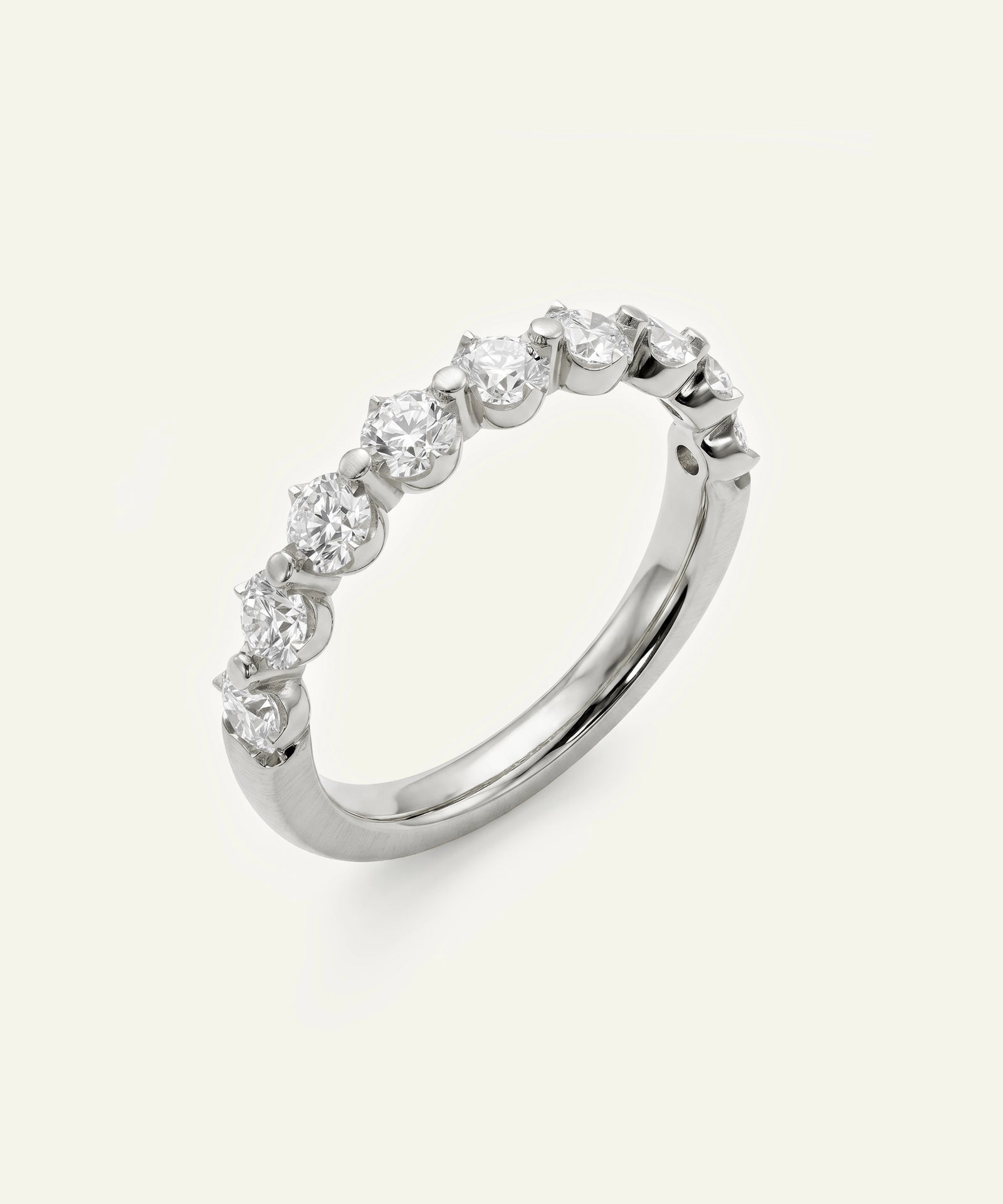 A silver-toned diamond eternity ring with multiple round-cut diamonds set in a continuous band, shown on a light cream background.