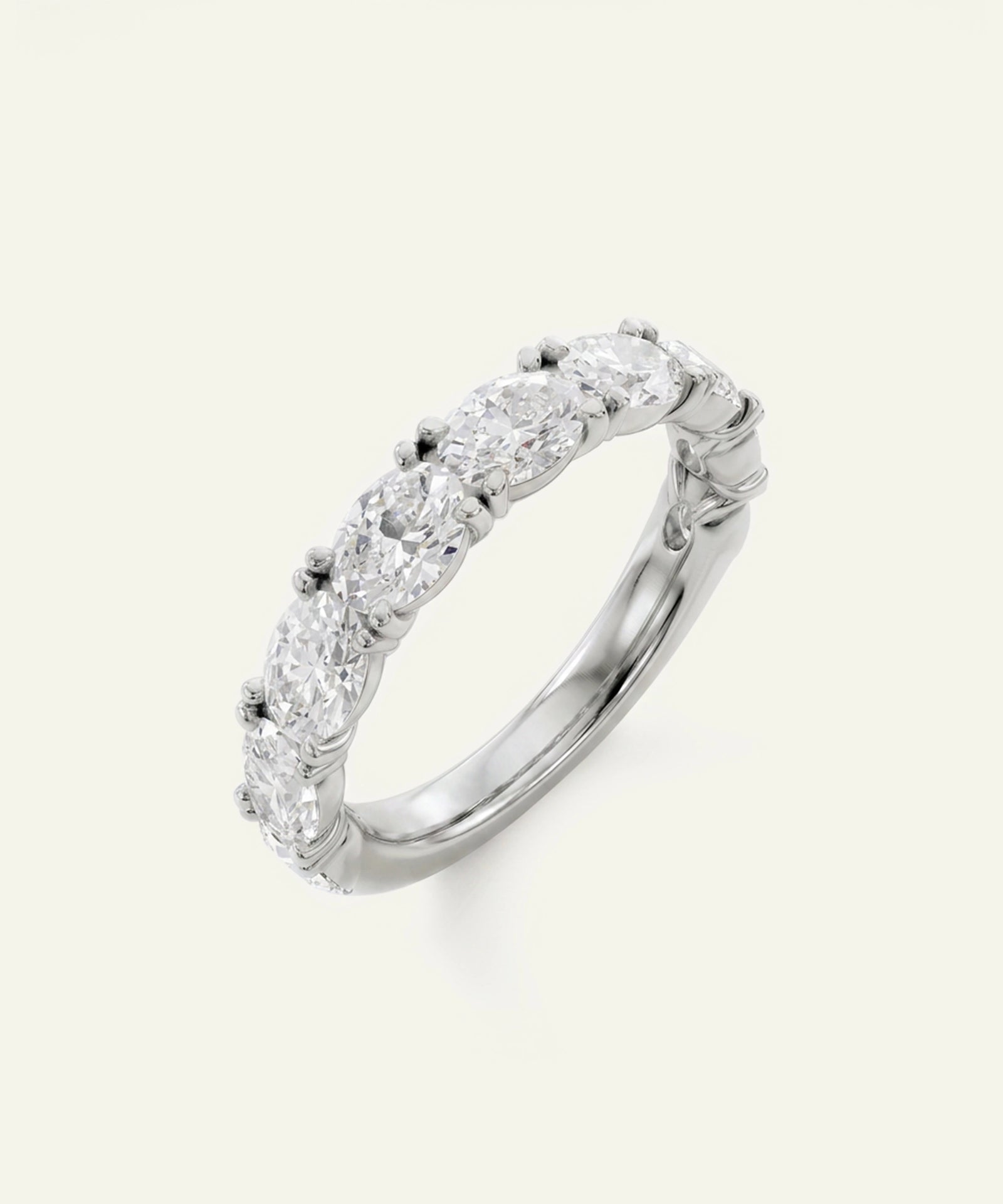 A silver-tone diamond eternity ring featuring a continuous row of round-cut diamonds in a prong setting, shown on a light cream background.
