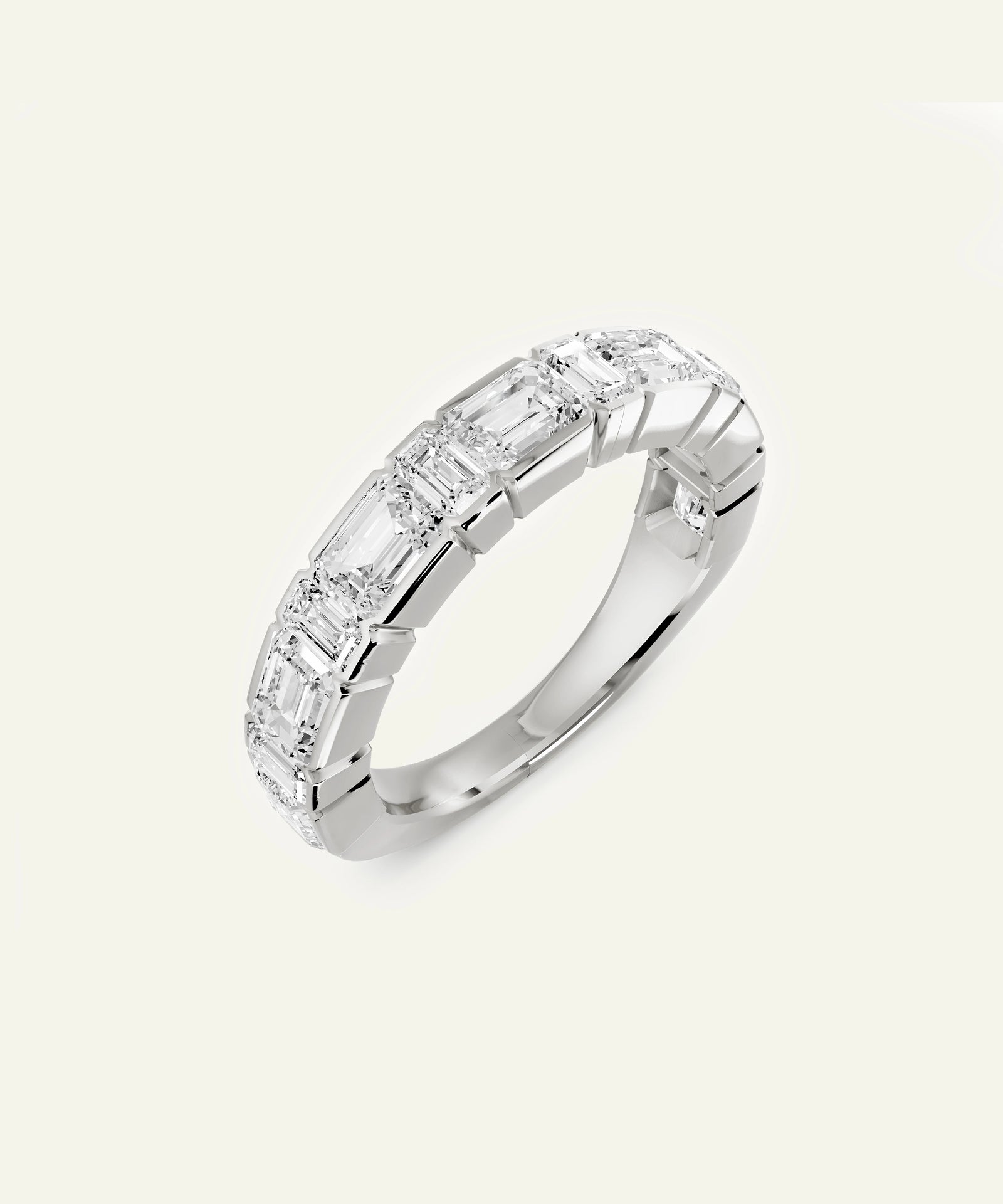 A silver band ring featuring a row of baguette-cut clear gemstones, shown on a light cream background.