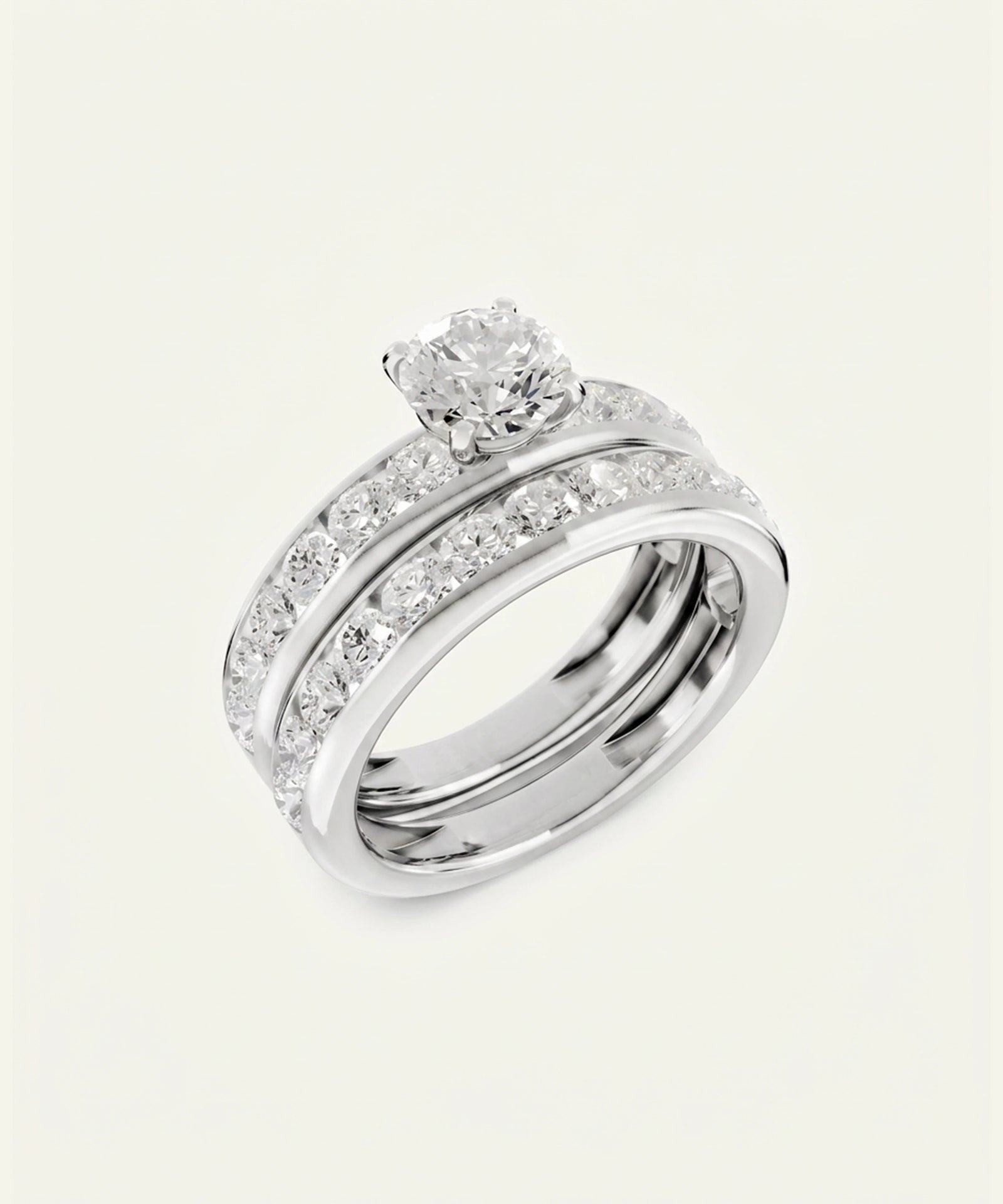 A silver-toned diamond engagement ring set with a round-cut center stone and a matching band featuring pavé-set diamonds, shown on a light cream background.