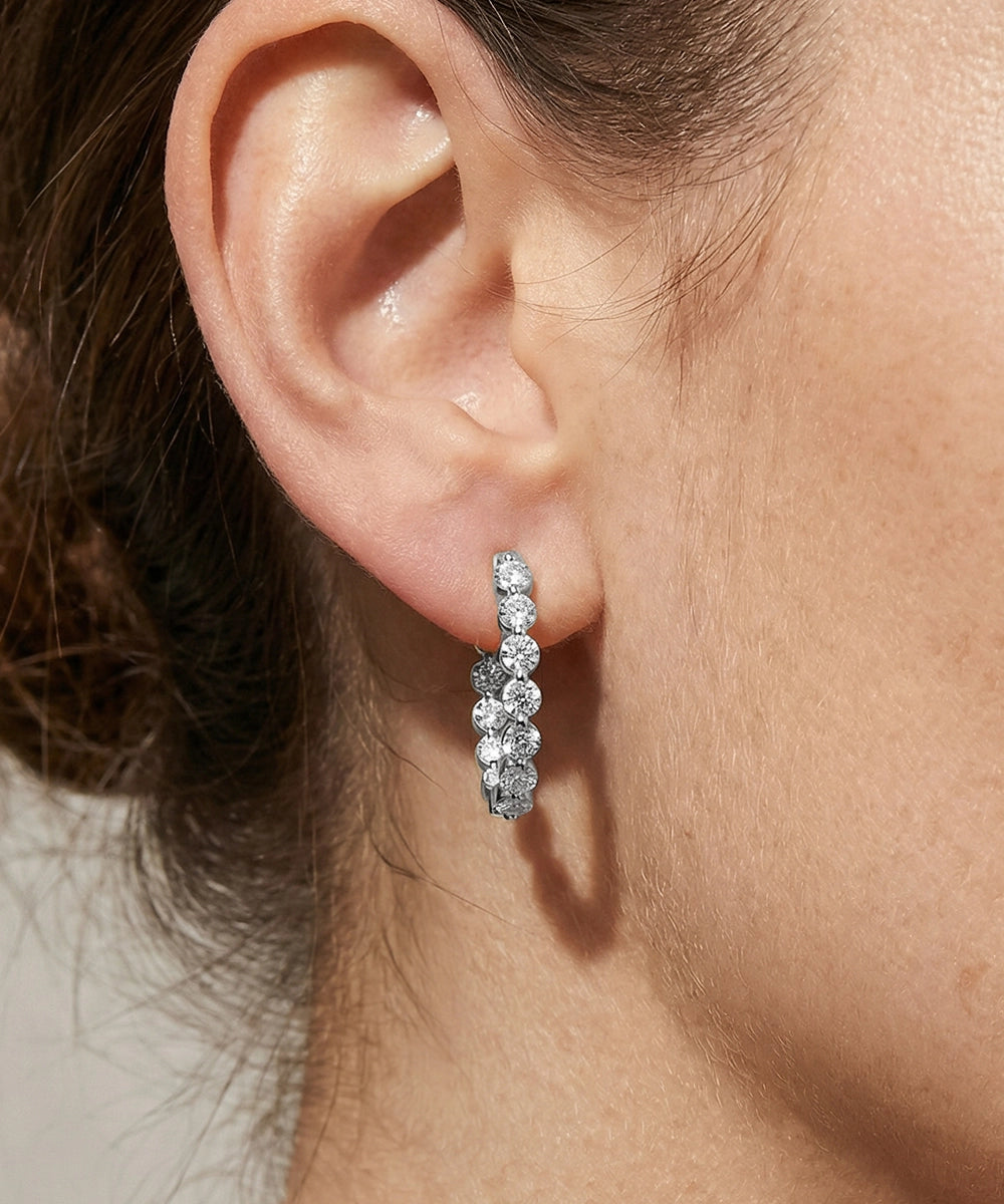 Close-up of an ear wearing a silver hoop earring with clear stones.